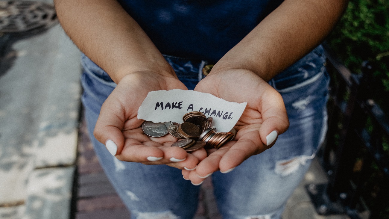 Foto de uma pessoa com as mãos abertas para cima, segurando moedas e um papel com o texto "make a change".