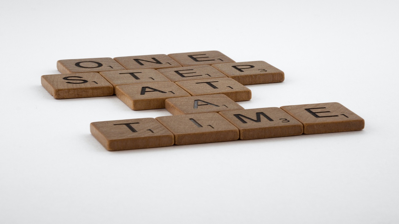 Peças de madeira com letras gravadas neles. Juntos, soletram as palavras "one step at a time", ou um passo de cada vez.