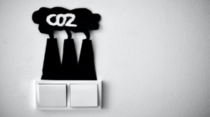 Interruptor de lâmpada. Acima, um recorte de papel no formato de usinas emitindo fumaça. Acima, o texto "CO2".