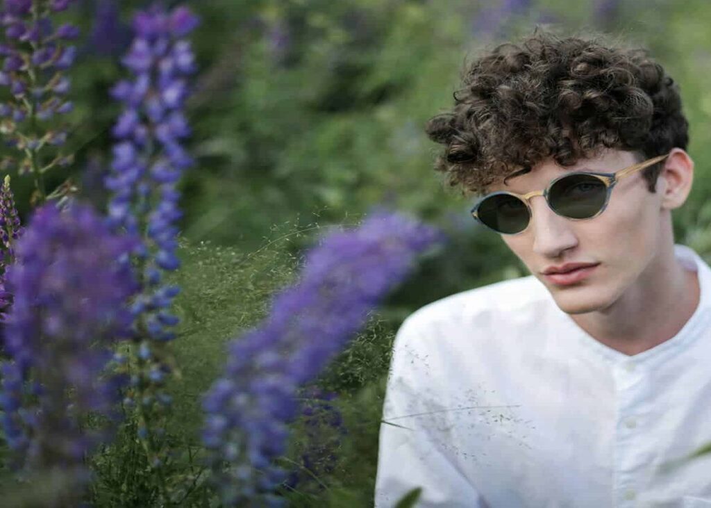 Foto de um campo de lavanda. No lado direito, um homem de camisa branca com óculos de sol sustentáveis da Praditto.